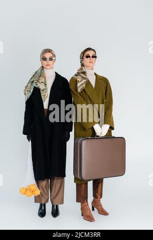 In voller Länge modische Frauen mit Retro-Koffer und frischen Orangen in Netztasche auf grauem Hintergrund Stockfoto