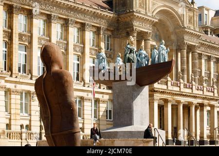 Ein großes öffentliches Kunstwerk, in dem der berühmte guyanesisch-britische Künstler Hew Locke die Skulptur der Königin Victoria im Stadtzentrum von Birmingham neu gestaltet. Das Projekt wurde von der Ikon Gallery für das Birmingham 2022 Festival (das Kulturprogramm der Commonwealth Games) in Auftrag gegeben. Das spektakuläre Werk mit dem Titel Foreign Exchange wird Lockes erste temporäre öffentliche Skulptur sein. Auf dem Bild sieht Anthony Gormleys Iron man-Statue auf Foreign Exchange zu. Stockfoto