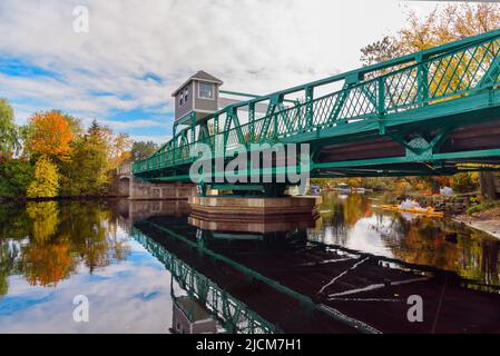 Schwingen Sie die Brücke über einen Fluss an einem teilweise bewölkten Herbsttag. Reflexion im Wasser. Stockfoto