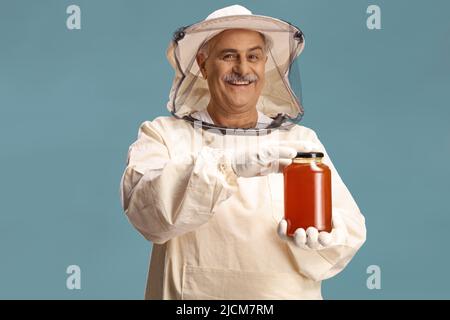 Bienenhalter in einer Uniform mit einem Honigglas isoliert auf blauem Hintergrund Stockfoto