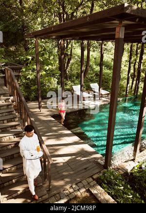 Ein Butler serviert einer Frau Drinks vor der Ganga Pool Villa in Ananda im Himalaya, dem Palace Estate, Narendra Nagar, Indien. Stockfoto