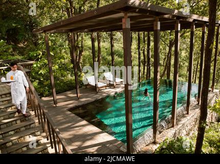 Ein Butler serviert einer Frau Drinks vor der Ganga Pool Villa in Ananda im Himalaya, dem Palace Estate, Narendra Nagar, Indien. Stockfoto