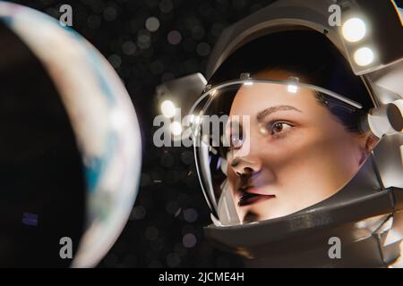 3D Darstellung einer konzentrierten jungen Astronautin in einem modernen grauen Raumanzug mit Blick auf den Planeten während der Weltraumexpedition Stockfoto