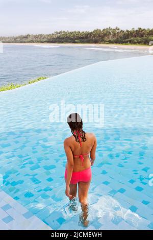 Eine junge Frau kommt in den Hauptpool mit Meerblick in Saman Villas, Aturuwella, Bentota, Sri Lanka. Stockfoto