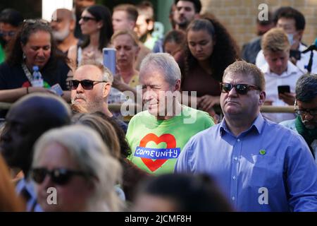 Auf einer Großleinwand am Fuß des Grenfell Tower in London beobachten die Menschen eine Zeremonie zur Festlegung von Glaubensbekenntnis und Kranz, um an die zu erinnern, die am 14 2018. Juni beim Feuer im Grenfell Tower ums Leben kamen. Bilddatum: Dienstag, 14. Juni 2022. Stockfoto