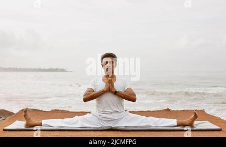 Der Sri-lankische Yogameister praktiziert Yoga am Strand. Aturuwella, Bentota, Sri Lanka; hier ist die sitzende, breibeinige Straddle-Pose zu sehen Stockfoto