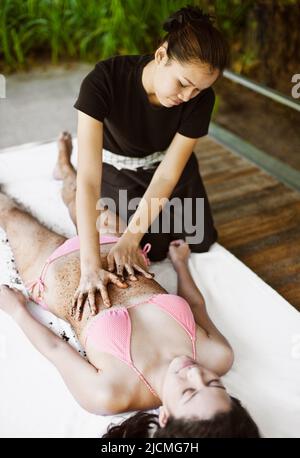Frau Erhält Kaffeeschrubben. Thailand. Eine Frau erhält ein Kaffee-Körperpeeling im Freien in einer Cabana am Pool. Stockfoto