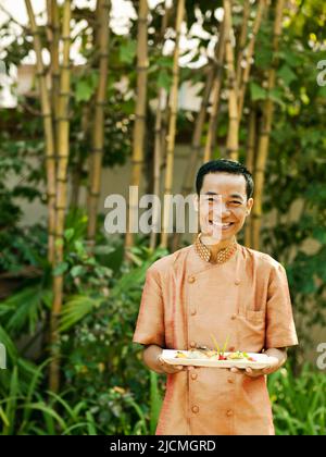 Ein asiatischer Kellner trägt Fischgerichte. Siem Reap, Kambodscha. Stockfoto