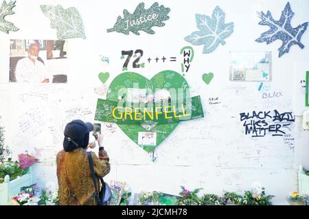 Ein Mitglied der Öffentlichkeit fotografiert das Denkmal am Fuße des Grenfell Tower in London, um an die Menschen zu erinnern, die am 14 2018. Juni beim Feuer im Grenfell Tower ums Leben kamen. Bilddatum: Dienstag, 14. Juni 2022. Stockfoto