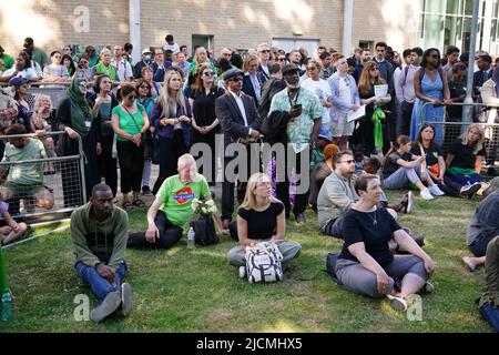 Auf einer Großleinwand am Fuß des Grenfell Tower in London beobachten die Menschen eine Zeremonie zur Festlegung von Glaubensbekenntnis und Kranz, um an die zu erinnern, die am 14 2018. Juni beim Feuer im Grenfell Tower ums Leben kamen. Bilddatum: Dienstag, 14. Juni 2022. Stockfoto