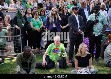 Auf einer Großleinwand am Fuß des Grenfell Tower in London beobachten die Menschen eine Zeremonie zur Festlegung von Glaubensbekenntnis und Kranz, um an die zu erinnern, die am 14 2018. Juni beim Feuer im Grenfell Tower ums Leben kamen. Bilddatum: Dienstag, 14. Juni 2022. Stockfoto