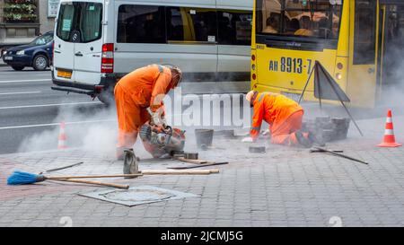 Straßenarbeiter legen Pflasterplatten. Eine mit einer Kreissäge schneidet Betonblöcke. Stockfoto