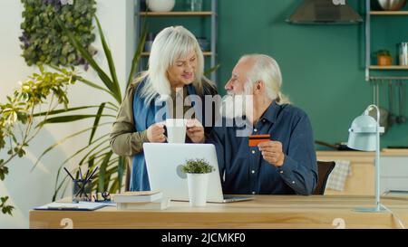 Aufgeregt glücklich ältere Paar Online-Shopping von zu Hause aus mit Computer und Kreditkarte. Online-Shopping, Warenauswahl zur Bestellung auf der Interne Stockfoto