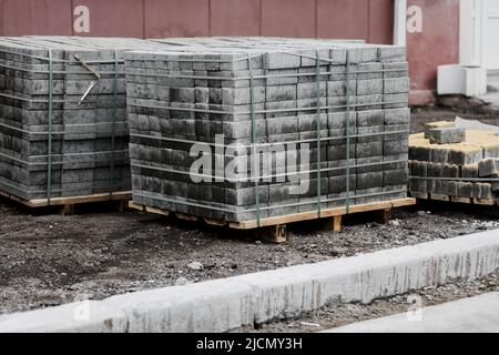 Neue Pflasterplatten ordentlich auf Paletten gestapelt. Fliesen auf dem Bürgersteig. Baustelle. Stockfoto