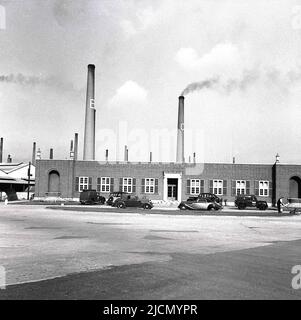 1950s, historisch, Außenansicht, Autos aus der Zeit, die vor der London Brick Company, Stewartby, Bedford, England, Großbritannien, geparkt wurden. Rauch kommt aus den berühmten großen Schornsteinen der Ziegelei. Stockfoto