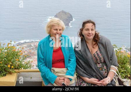 Porträt von Mutter und Tochter, die auf einer Brüstung über der Stadt Garachico auf der Insel Teneriffa am bewölkten Morgen sitzen, Kanarische Inseln, Spanien. Stockfoto
