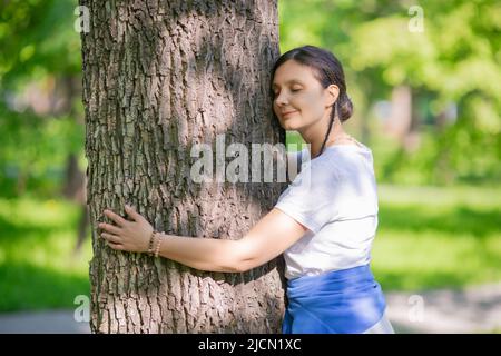 Eine 35-jährige Frau umarmt einen Baum. Das Konzept der Liebe zur Natur und des Energieaustauschs. Stockfoto