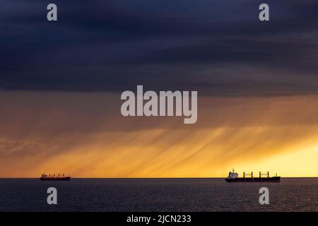 Rostock, Deutschland. 14.. Juni 2022. Vor dem Hafen von Rostock liegen Frachtschiffe auf den Straßen. Am Horizont ziehen Regenwolken vor der tiefen Abendsonne über die Ostsee. Quelle: Jens Büttner/dpa/Alamy Live News Stockfoto