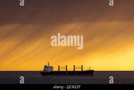 Rostock, Deutschland. 14.. Juni 2022. Das Frachtschiff 'Dema' liegt vor dem Hafen von Rostock vor Anker. Am Horizont ziehen Regenwolken vor der tiefen Abendsonne über die Ostsee. Quelle: Jens Büttner/dpa/Alamy Live News Stockfoto