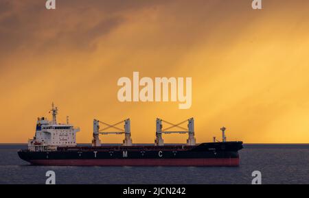 Rostock, Deutschland. 14.. Juni 2022. Das Frachtschiff 'Dema' liegt vor dem Hafen von Rostock vor Anker. Am Horizont ziehen Regenwolken vor der tiefen Abendsonne über die Ostsee. Quelle: Jens Büttner/dpa/Alamy Live News Stockfoto