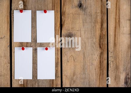 Leere Visitenkarten vor einem hölzernen Hintergrund. Vier Rechtecke aus weißem Papier, die mit Stecknadeln an alten Brettern befestigt sind. Selektiver Fokus. Stockfoto