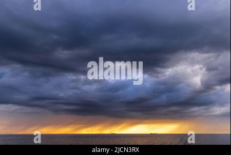 Rostock, Deutschland. 14.. Juni 2022. Vor dem Hafen von Rostock liegen Frachtschiffe auf den Straßen. Am Horizont ziehen Regenwolken vor der tiefen Abendsonne über die Ostsee. Quelle: Jens Büttner/dpa/Alamy Live News Stockfoto