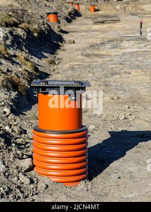 Neuer Sturmwasserbrunnen mit schwarzer Eisenrostabdeckung und braunem Kunststoff-Kanalrohr auf einer neuen Straßenbaustelle Stockfoto