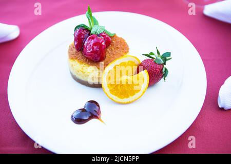 Mit Erdbeeren und Orange dekorierter Kuchenkuchen liegt auf einem weißen Teller Stockfoto