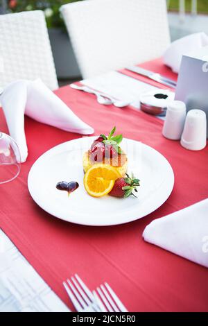 Mit Erdbeeren und Orange dekorierter Kuchenkuchen liegt auf einem weißen Teller Stockfoto
