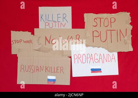 Papierschilder mit Slogans stoppen Krieg, russischen Mörder, Propaganda, Mörder Putin, stoppen Putin, Kein Krieg auf rotem Hintergrund, Protestaktion 2022 Stockfoto