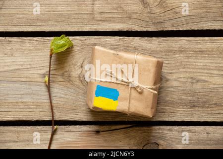 Eine Kiste mit einer gelb-blauen Flagge der Ukraine auf einem Holztisch, humanitäre Hilfe für die Ukraine, Postpaket und Lieferung Stockfoto