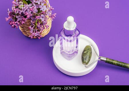 Serumflasche und Jade-Gesichtswalze auf weißem Teller auf violettem Hintergrund. Naturkosmetik, Hautpflege, Home Spa-Konzept. Draufsicht. Stockfoto