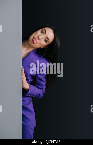 Grimazende Frau in purpurfarbenem Anzug, die die Zunge aus der Ecke herausstreckt. Stockfoto