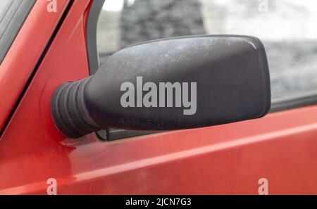 Linker Rückspiegel aus schwarzem Kunststoff auf einem roten Auto. Außenspiegel auf der Fahrerseite bei einem alten Auto Stockfoto
