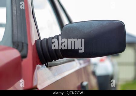 Linker Rückspiegel aus schwarzem Kunststoff auf einem roten Auto. Außenspiegel auf der Fahrerseite bei einem alten Auto Stockfoto