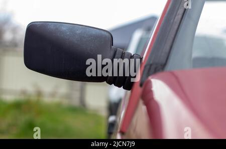 Linker Rückspiegel aus Kunststoff auf einem roten Auto. Außenspiegel auf der Beifahrerseite bei einem alten Fahrzeug Stockfoto