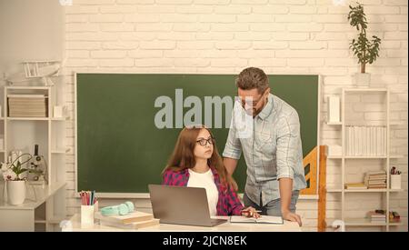 Neugieriges Kind und Vater sitzen im Klassenzimmer mit Computer an der Tafel, Kindheit Stockfoto