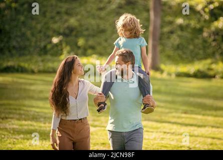 Elternschaft erfordert Liebe. Eltern und Kind im Sommer im Freien. Pflege Eltern und Sohn. Mutter und Kind reiten auf dem Schweinchen auf dem Vater. Adoptivfamilie. C Stockfoto