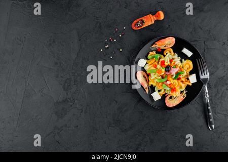 Mehrfarbige Pasta mit Garnelen auf schwarzem Beton-Hintergrund. Stockfoto