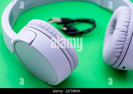 Kabellose Nahaufnahme-Kopfhörer mit einem auf grünem Hintergrund isolierten USB-Ladekabel. Stockfoto