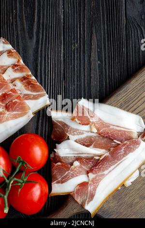 Parmaschinken auf dunklem Holzboden mit Tomate, Draufsicht, flach liegend Stockfoto
