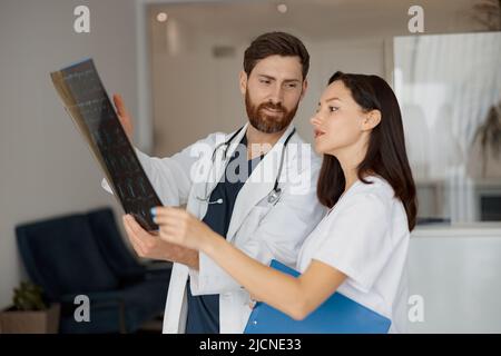 Zwei Ärzte in Uniform schauen und diskutieren einen Scan der Wirbelsäule des Patienten Stockfoto