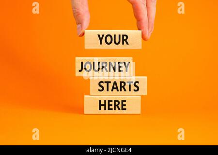 Ihre Reise beginnt hier Symbol. Konzeptworte Ihre Reise beginnt hier auf Holzblöcken auf einem wunderschönen orangen Tisch mit orangefarbenem Hintergrund. Business, moti Stockfoto