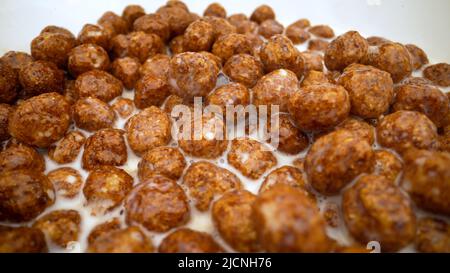 Schokolade Flocken werden mit Milch gegossen. Super close up. Milch wird in Frühstücksflocken Schokolade Maiskugeln gegossen. Milch mit Chocola in die Schüssel gießen Stockfoto