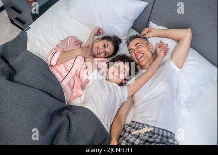 Eine nette Familie, die im Bett lag, lächelte und sah fröhlich aus Stockfoto
