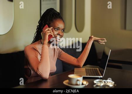 Wütende, schreiende Frau mit gemischter Rasse, Influencer trinkt Kaffee, telefoniert, arbeitet online im Café mit Laptop, PC Stockfoto