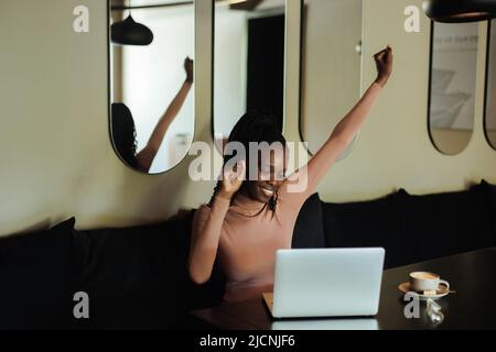 Froh erfolgreiche und stolze interracial afro amerikanische Geschäftsfrau auf Remote-Arbeit im Café. Den Arm heben, den Sieg Stockfoto