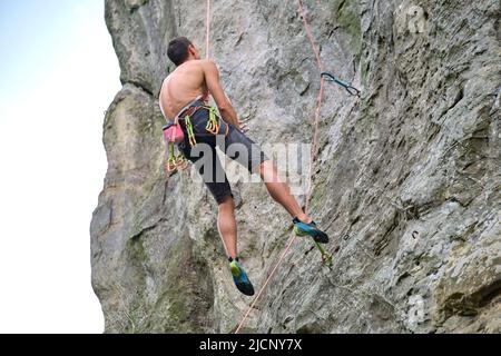 Entschlossener Kletterer, der die steile Wand des felsigen Berges hochklettert. Sportler überwinden schwierige Route. Extremsport und Klettern Stockfoto