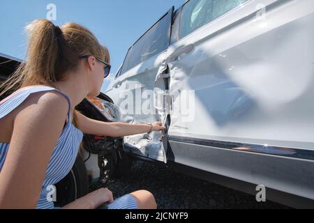 Traurige weibliche Fahrerin, die auf der Straßenseite saß, war nach einem Autounfall schockiert. Konzept der Straßenverkehrssicherheit und Fahrzeugversicherung Stockfoto