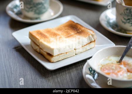 Orientalisches, traditionelles hainanesisches Frühstück mit Toastbrot, halbgekochten Eiern und Kaffee. Stockfoto